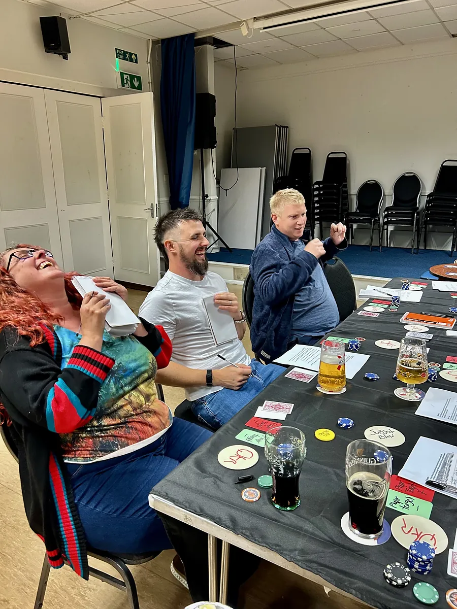 Three players at a Quoker table, one laughing with her head thrown back as another punches the air.